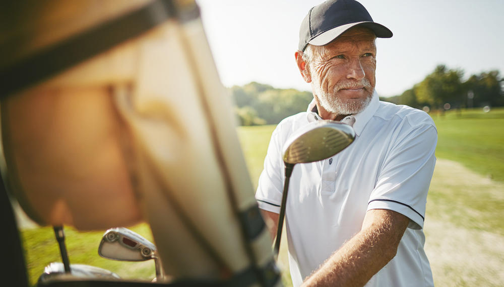 Skjønn eldre mann med golfkøller på en golfbane